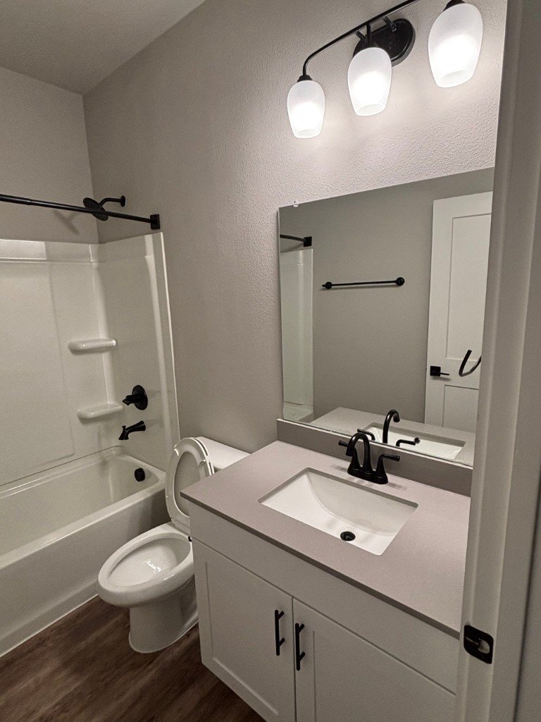 Renovated bathroom with white vanity, tub-shower alcove, matte black fixtures, and wood-look flooring