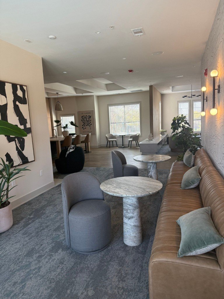 Finished lounge and common area with seating, lighting, and kitchen in the background